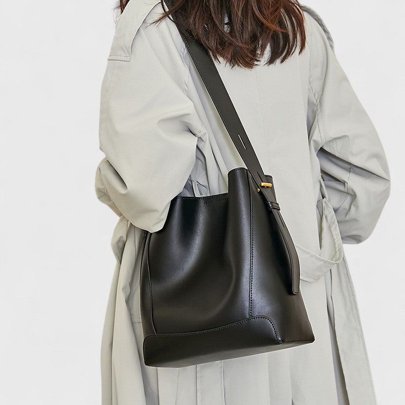 Vue de dos d’une femme portant un sac messager noir en cuir avec longue bandoulière réglable.
