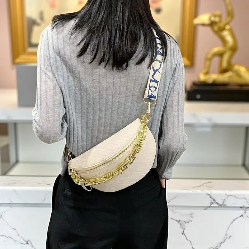 Sac de poitrine femme en cuir synthétique blanc avec chaîne dorée porté en travers.