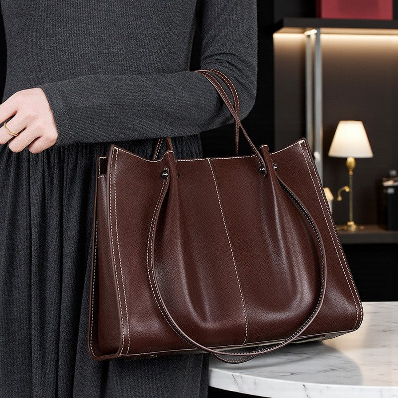 Femme habillée en noir portant un sac en cuir marron à double anse arrondie.