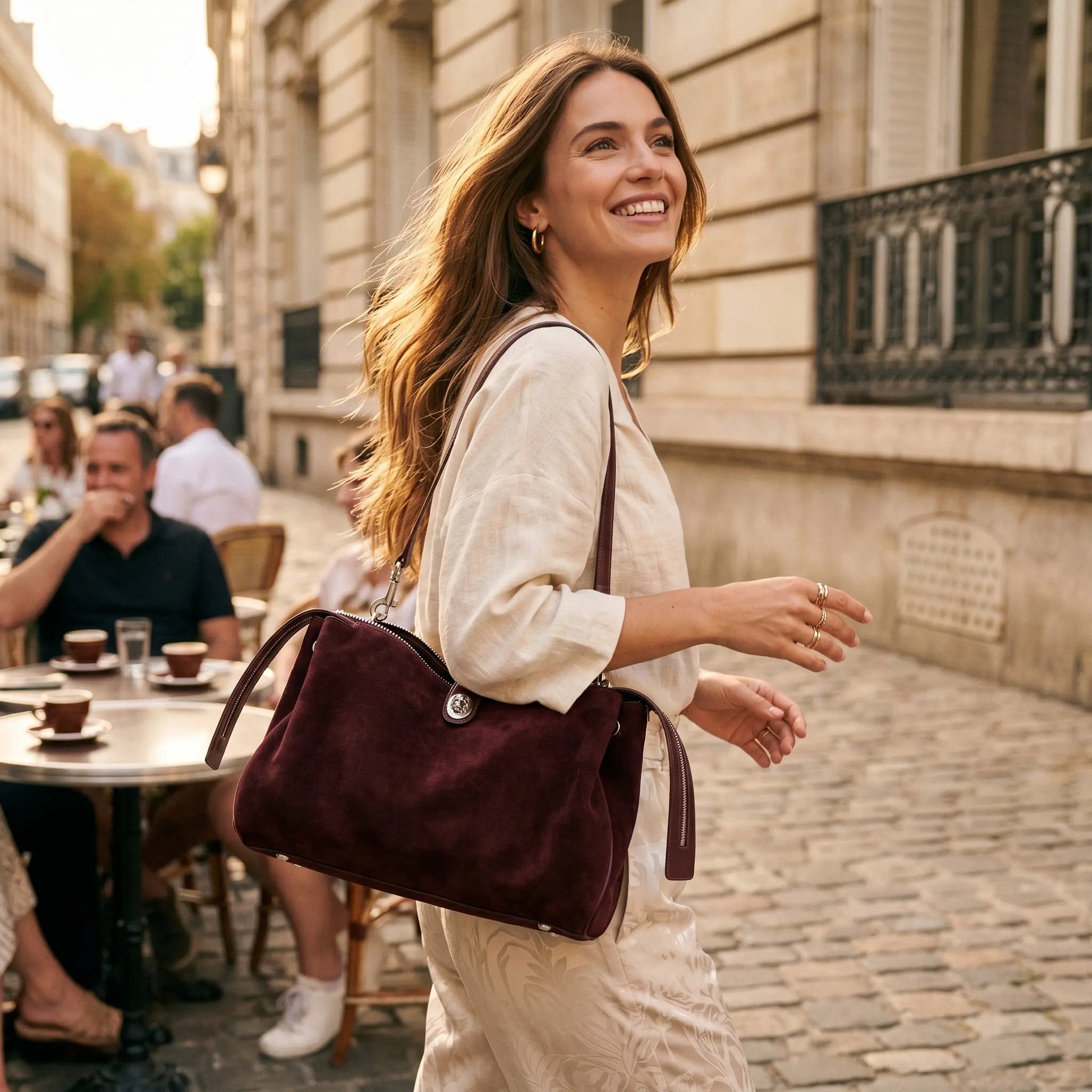 Sac porté épaule en cuir suédé prune porté par une femme dans une rue pavée avec terrasse de café